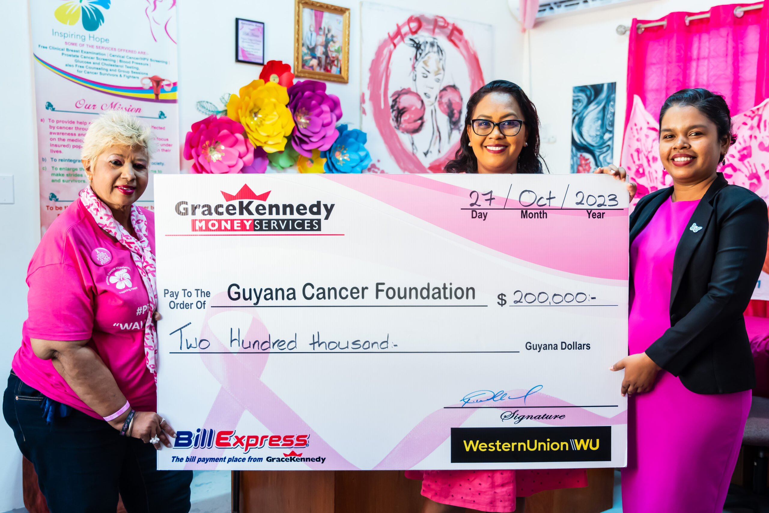 Tina Seabra-Gibson and Margo Boodoo, Marketing Officer and Customer Service Representative of GKMS hand over the cheque to Founder and President of the Guyana Cancer Foundation, Bibi Hassan, holding the cheque.